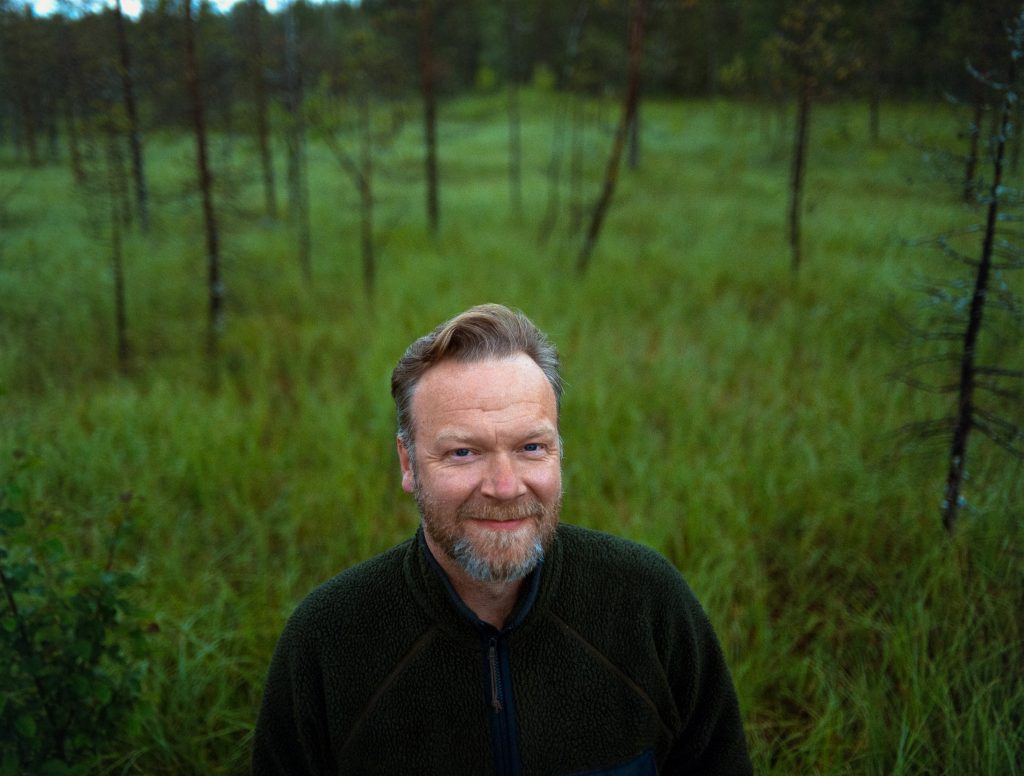 Eemil Karila smiles at the camera wearing a green fleece jacket in the forest, Rovaniemi