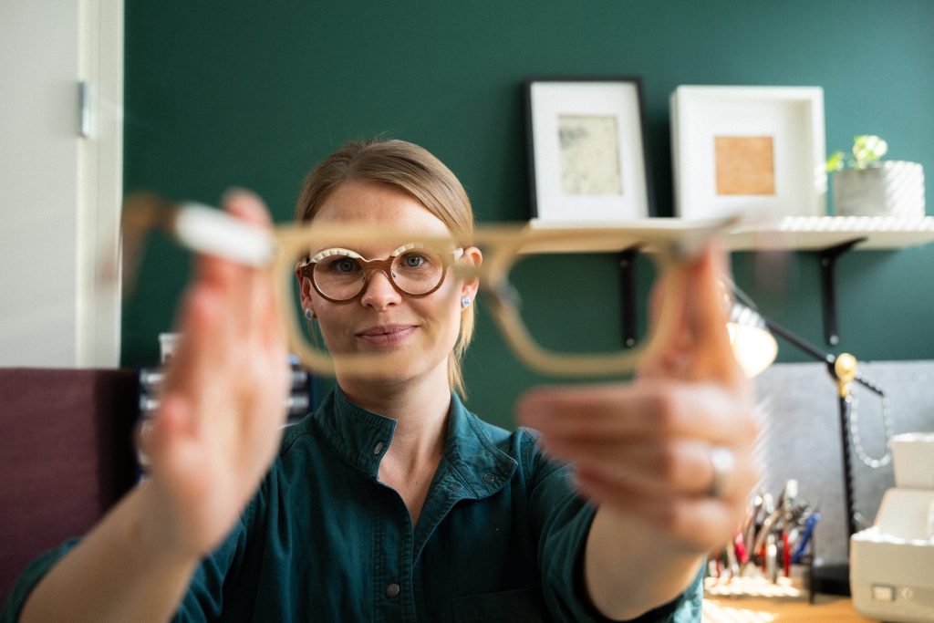 Laura Knuuti holds wooden-framed glasses up to the camera, Sodankylä