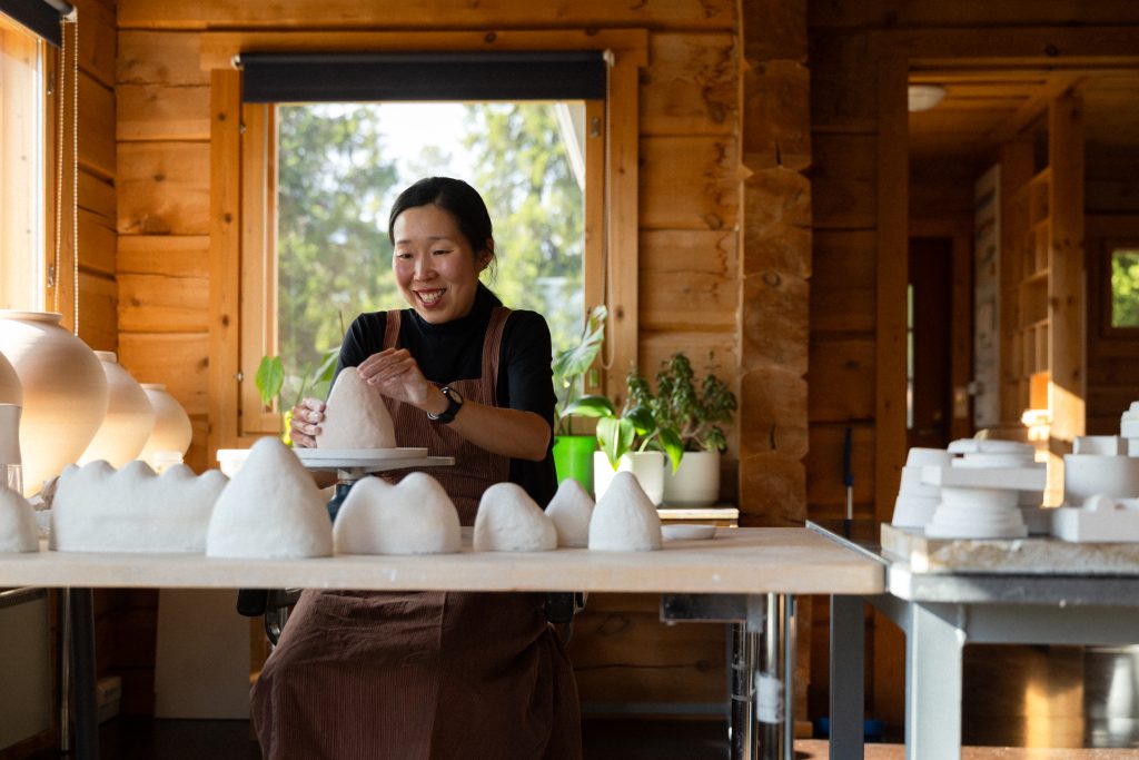 Miki Kim shapes clay in her ceramics studio, smiling, Posio