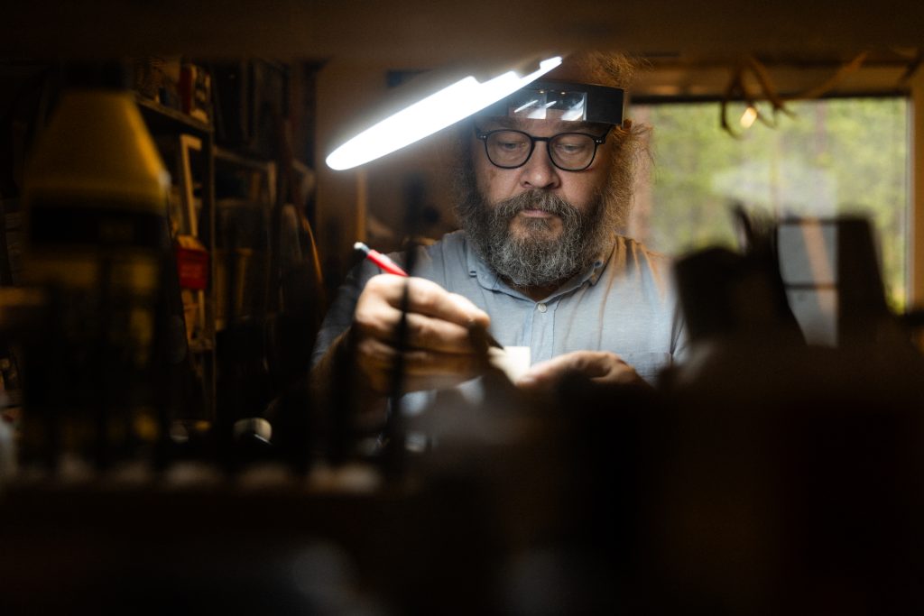 Pasi Jaakonaho does precise handwork in his workshop under a magnifying lamp, Inari
