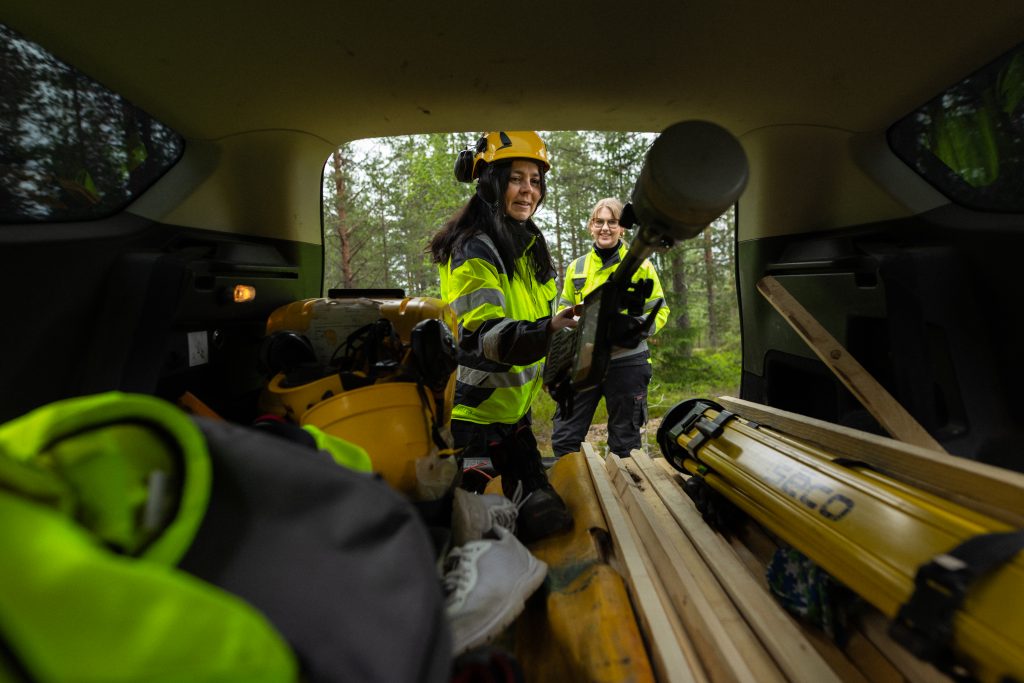 Measuring equipment in a car boot, two workers in hi-vis vests in the background